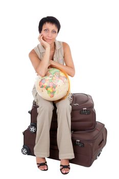 Smiling young tourist haircut woman dressed buff trouser suit sits on the  brown traveling suitcase with globe isolated