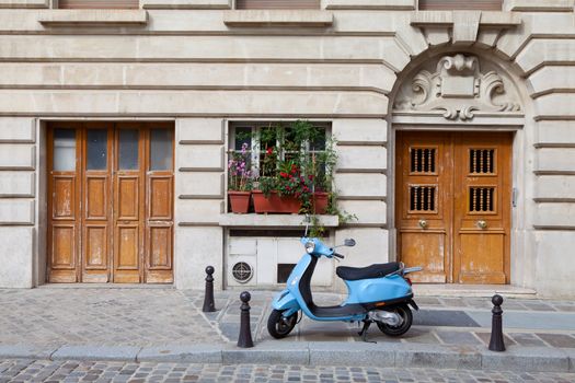 Blue retro motor bicycle parked between two wooden doors on sidewalk near old style house and cobblestone street in European town