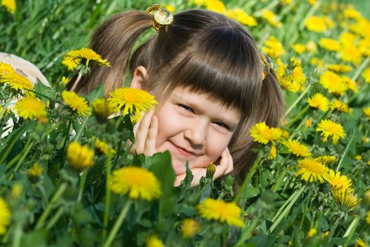 Little cool smiling girl is lying on the flowering dandelion meadow