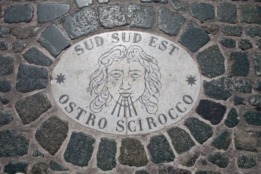 Sign on marble board of wind sud sud est ostro scirocco embedded in granite cobblestone on St. Peter’s square in Vatican Rome Italy