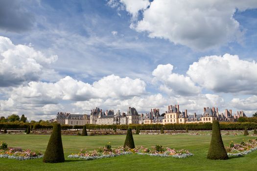 Medieval landmark royal hunting castle Fontainbleau near Paris in France and garden with flowers on the cloudy blue sky background