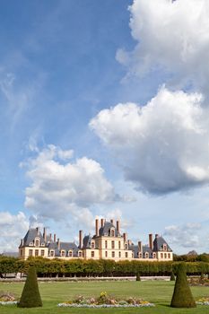 Medieval landmark royal hunting castle Fontainbleau near Paris in France and garden with flowers on the cloudy blue sky background