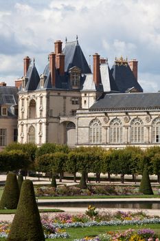 Medieval landmark royal hunting castle Fontainbleau near Paris in France and garden with flowers on the cloudy blue sky background