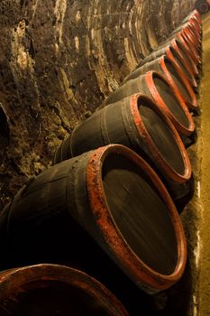 Row of Old wine barrels are stored in winery cellar near aged wall resedes into the distance