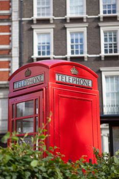 Traditional London symbol red public phone box on green park and residential district background, Great Britain