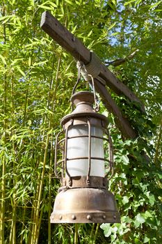 Street aged vintage copper kerosene oil lamp with glass bulb is hung up batten outside on the green leaves background