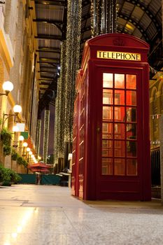Traditional London symbol red public phone box for calling in illuminated and festively decorated empty trade passage in evening. Great Britain