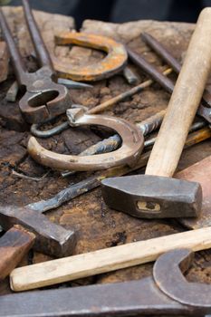 Rusty blacksmith tools and horseshoes on wooden log