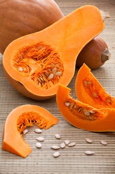 Ripe orange gourds and half, sliced fleshy segments and white seeds on rural straw woven surface and stripy background