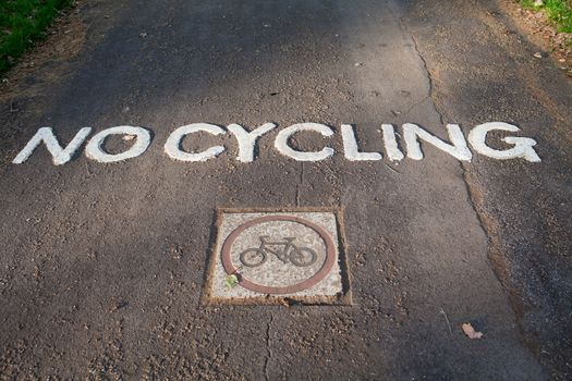 White engraved painted traffic sign “no cycling” and bike on park gray asphalt pathway