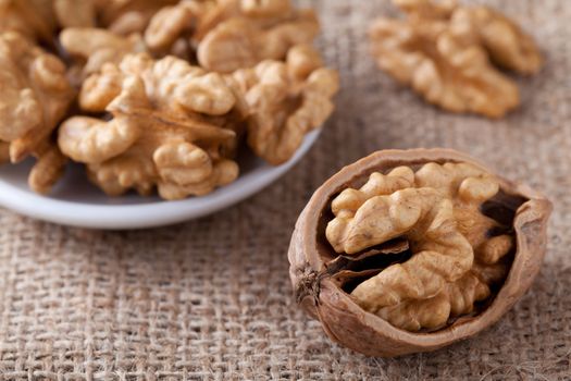 Cores of matured nuts in plate and cracked brown Circassian walnut close-up on the sackcloth background