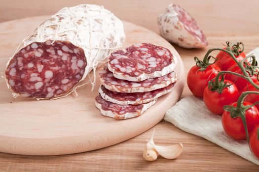 Traditional sliced salami on wooden board with garlic, cherry tomatoes