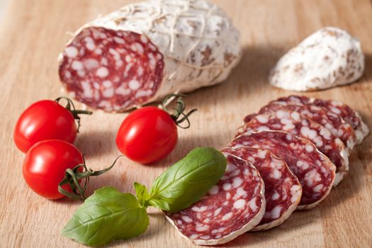 Traditional sliced meat sausage salami on wooden board with basilic and red bunch of cherry tomatoes