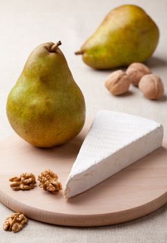 Ripe green pears, piece of white soft cheese brie, cores of Circassian walnuts on wooden board and linen tablecloth