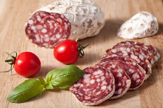 Traditional sliced meat sausage salami on wooden board with basilic and red bunch of cherry tomatoes