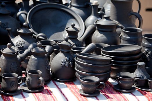 Rustic handmade black ceramic pottery souvenirs (plates, bowls, teapots, cups) on embroidered traditional Ukrainian towel at street handicraft market