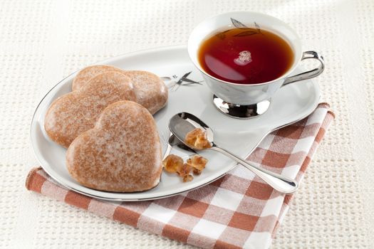 Served cookies heart shape, crystal brown sugar in silver spoon, black tea in cup on saucer on plaid textile tablecloth