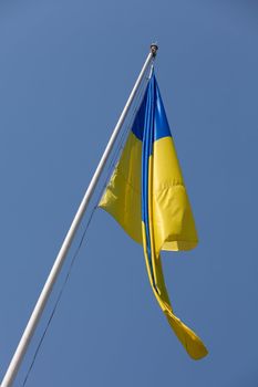 Waving Ukrainian Yellow-Blue Flag hoisted on flagpole on the blue sky background