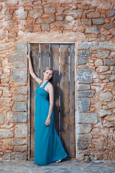 Portrait of romantic gentle elegant young blond woman with blue eyes and dress on the Mediterranean style court, wooden door and  stone wall background