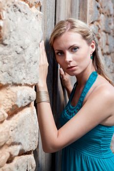 Portrait of romantic gentle elegant young blond woman with blue eyes and dress on the Mediterranean style court, wooden door and  stone wall background