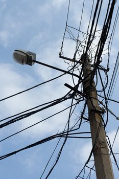 Lamp pole and tangled electric wires on the blue sky background. Vertical