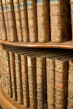 Hard covers of rust old medieval literary books on wooden shelves in bookcase