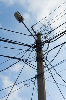 Lamp pole and tangled electric wires on the blue sky background. Vertical