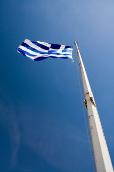 Flying Greek Flag hoisted on flagpole on the blue sky background