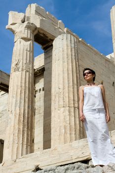 Close-up young woman dressed white near the columns of entrance propylaea to ancient temple Parthenon in Acropolis Athens Greece on blue sky background