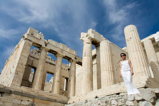 Young woman dressed white near the columns of entrance propylaea to ancient temple Parthenon in Acropolis Athens Greece on blue sky background