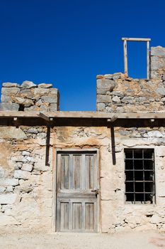 Picturesque old Mediterranean style abandoned lopsided rustic stone house with padlocked wooden door and window lattice on blue sky background