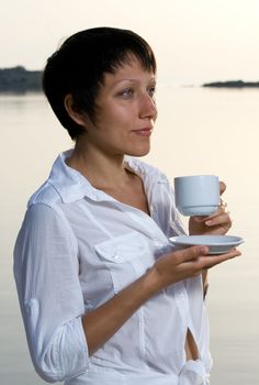Young dressed white brunette woman meets sunrise drinking morning coffee