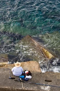 Fisherman in hat is sitting on the stone and fishing, top vertical view