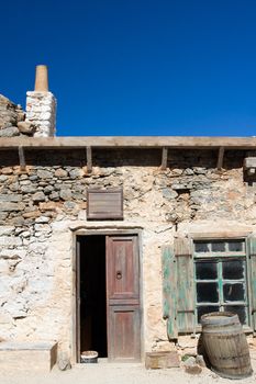 Picturesque old Mediterranean style abandoned lopsided rustic stone coffee house with opened wooden sun blind, chimney,  doorway, wine barrel and bench on the blue sky background