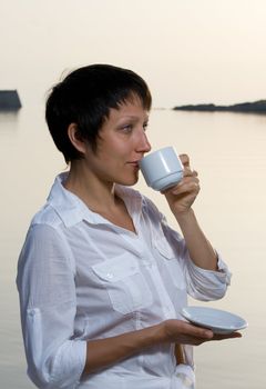 Young dressed white brunette woman meets sunrise drinking morning coffee