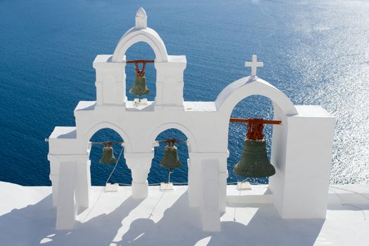 View on calm sea surface through traditional Greek white church arch with cross and bells in village Oia of Cyclades Island Santorini Greece