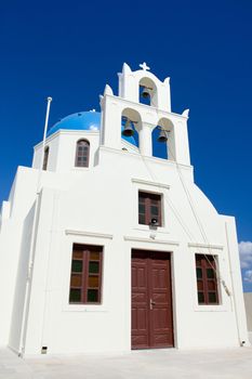 Entrance in traditional Greek white church, archs with cross and bells in village Oia of Cyclades Island Santorini Greece