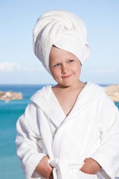 Portrait of happy smiling little girl with towel on the head in white bathrobe relaxing on terrace on the sea background