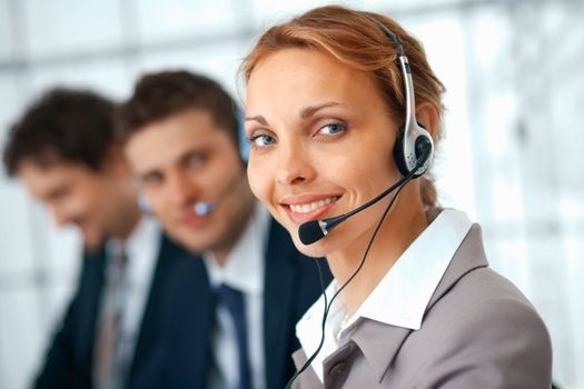 Closeup of a businesswoman with headset, her colleagues at the background.