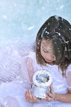 Little angel in the snow holds a snow globe and watches the earth. Elements of this image furnished by NASA.