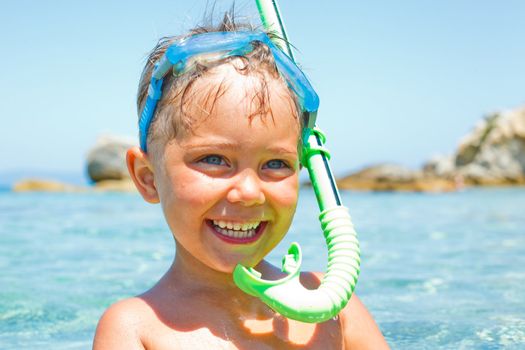 Cute boy in swimming goggles and snorkel swimming in the transparent sea