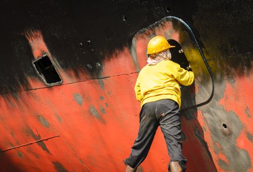 Worker cleaning side of ship at shipyard