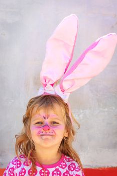 Girl dressed up as an easter rabbit with rabbit ears and facepaint. Smiling at the camera, happy feeling. Space for text