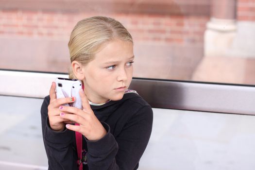 Child sitting outdoors with a smart phone, looking away from the camera. Space for text