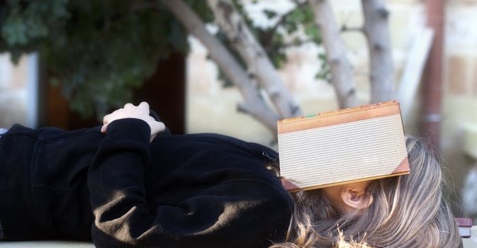 A student lying outside with a book covering her face