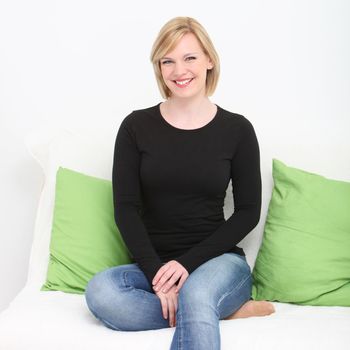 Barefoot smiling vivacious woman sitting on a couch with her leg tucked up under her in jeans