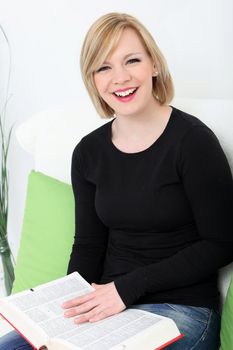 Closeup portrait of an attractive young laughing woman sitting on a couch enjoying a large book