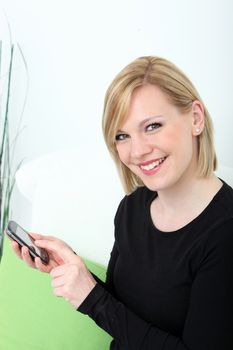 Smiling friendly young woman sending a text message on her mobile phone typing in the information on the touchscreen with her finger