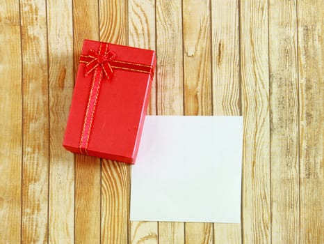 Red present box with blank note paper on wooden background 