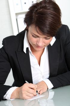 An attractive brunette businesswoman sitting at her desk, concentrating on making some notes